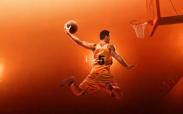 Young muscular basketball player with a ball on floodlight professional court scoring a goal