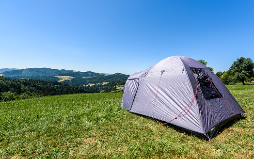Camping tourist tent set up on meadow in the mountains. Small tent in green mountains of Slovenia. Discovering, hiking on active family vacation in nature with spectacular view of hills and forest.