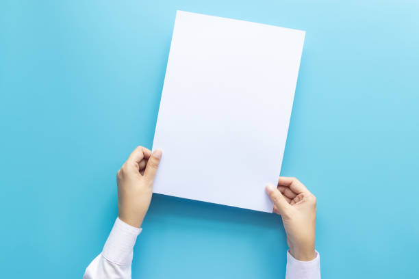 istock close up hands holding  empty white blank letter paper size A4 for flyer or invitation mock up isolated on a blue background. 1164104510
