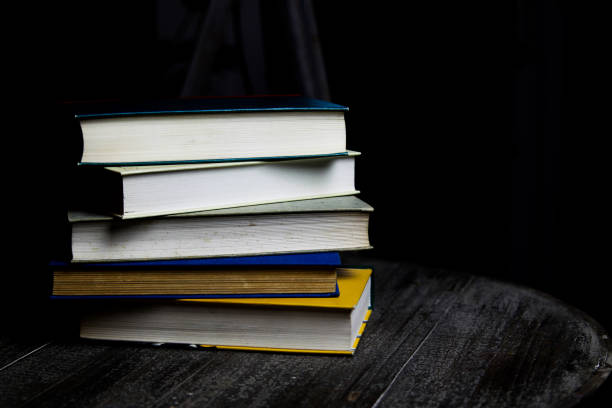 istock Stack of old books on round wood table with reading light during night 1164104602