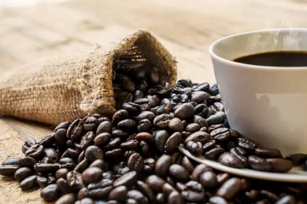 Closeup of coffee beans with cup and bag on the wooden table