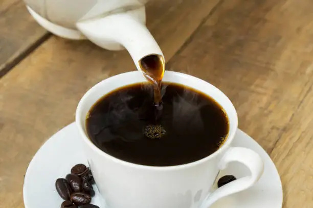 Closeup of aromatic coffee pouring into the cup on the wooden table