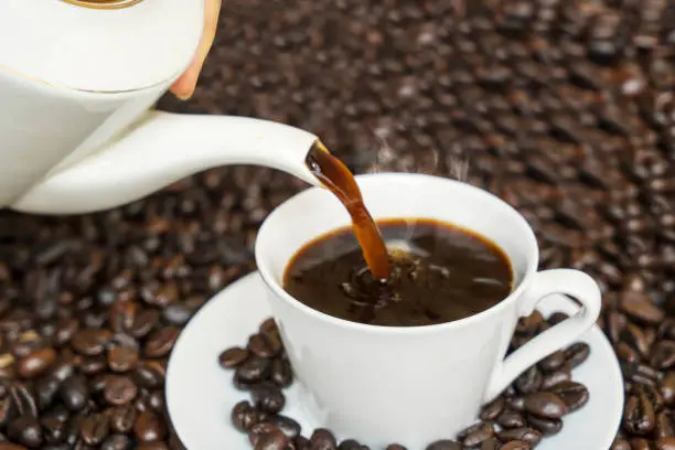 Closeup of hot coffee pouring into the white cup with coffee beans background