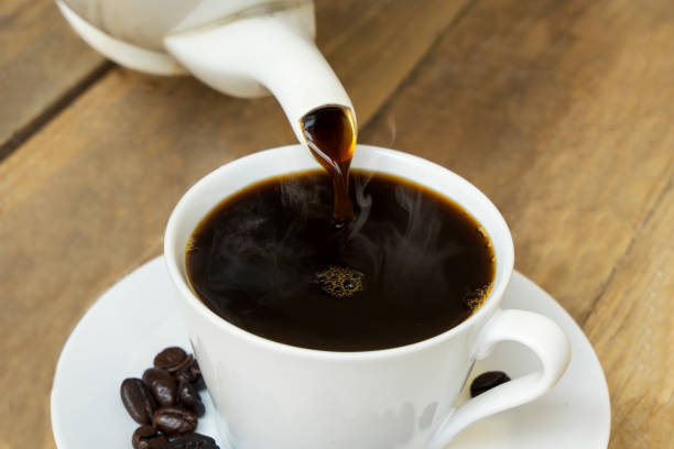 istock Tasty coffee pouring into white cup on table 1164104813