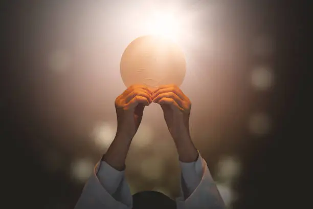Close up of pastor praying to God while lifting a bright communion bread in the dark background