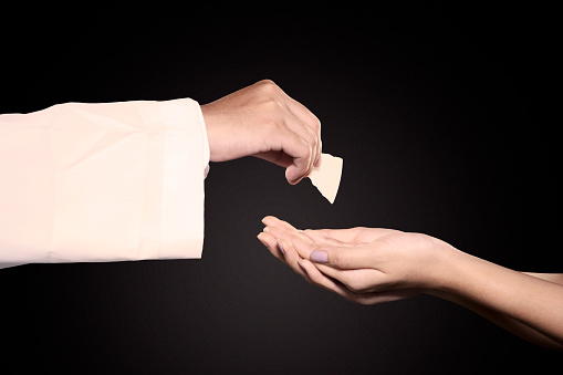 Close up of pastor giving first communion bread on woman hands in dark background