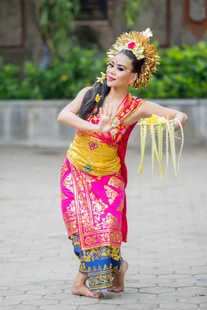 Picture of young Balinese dancer dancing Pendet dances with a bowl of flower petals at outdoor