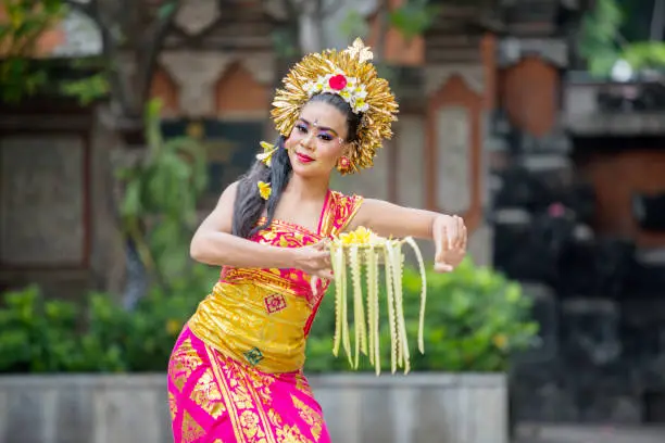 Beautiful dancer dancing Pendet dances with a bowl of flower petals at outdoor