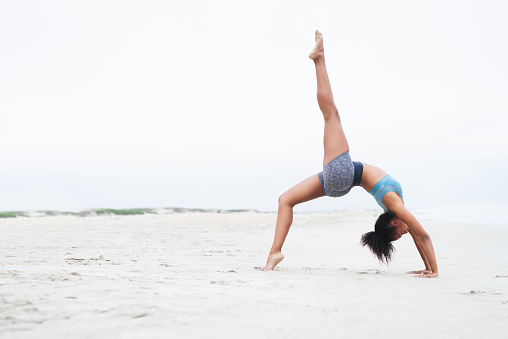 Shot of a young woman doing a handstand at the beach