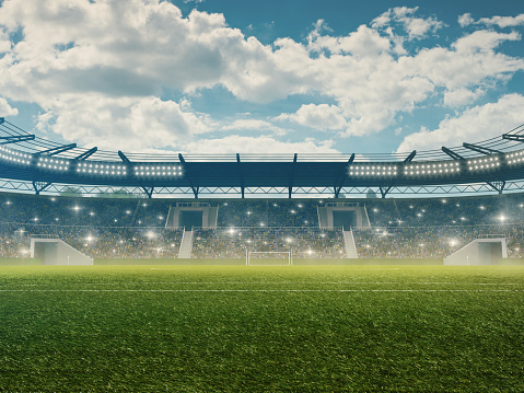 Professional soccer stadium with tribunes, illumination, green grass and cloudy blue sky