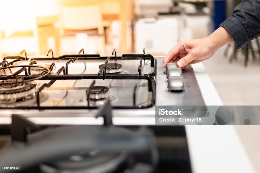 Male hand turning switch knob on gas stove Male hand turning switch knob on modern gas stove in kitchen showroom. Cooking appliance in domestic kitchen. Home improvement and House interior design concepts Natural Gas Stock Photo