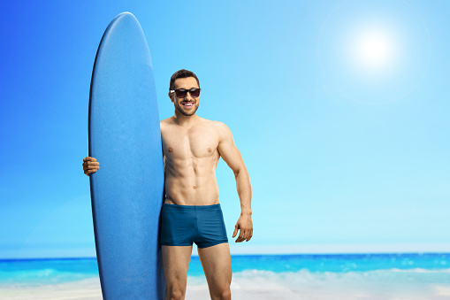 Young handsome man with a surfboard at a beach smiling at the camera