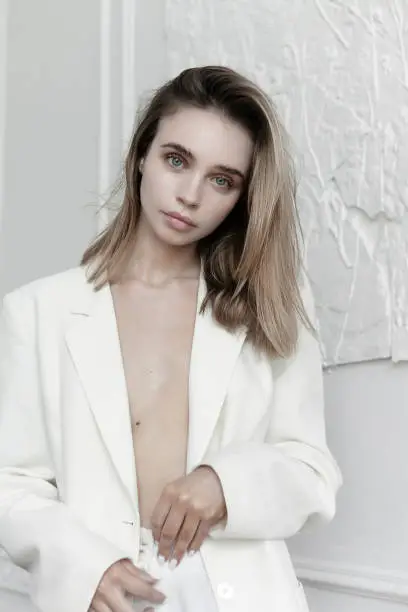 Beautiful young woman pf upper class wearing white suit: pants and blazer designer clothing looking beautiful confident with natural professional make-up on the Parisian apartment background Luxury lifestyle concept