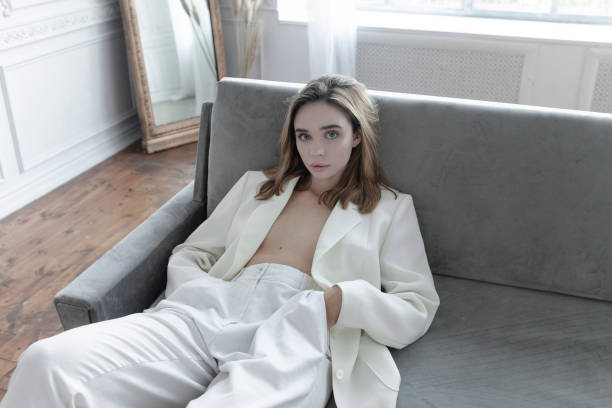 Luxury lifestyle Beautiful young woman in Parisian apartment Looks gorgeous Luxury lifestyle Beautiful young woman wearing white suit: pants and blazer in Parisian apartment Looks gorgeous Fresh natural make-up Fashion model lying or sitting on the gray color sofa Amazing vintage style interiour designer clothing photos stock pictures, royalty-free photos & images
