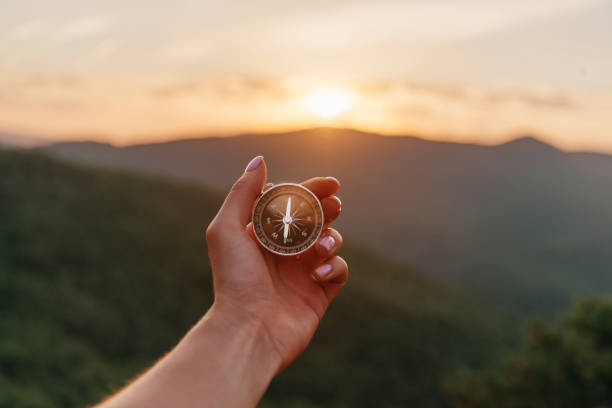 Female hand with compass in summer mountains at sunrise, pov. Explorer young woman holding compass in hand in summer mountains at sunrise, point of view. Concept of hiking and travel. orienteering stock pictures, royalty-free photos & images