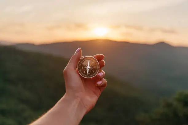Photo of Female hand with compass in summer mountains at sunrise, pov.