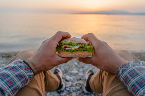 Young man resting with burger by the sea, pov.