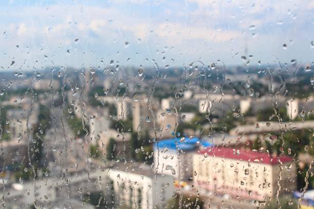 istock Rain drops falling on building window against city tower background on a sunny day 1164123812