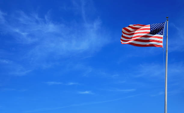 istock waving American flag at tall flagpole over clear blue sky 1164127818