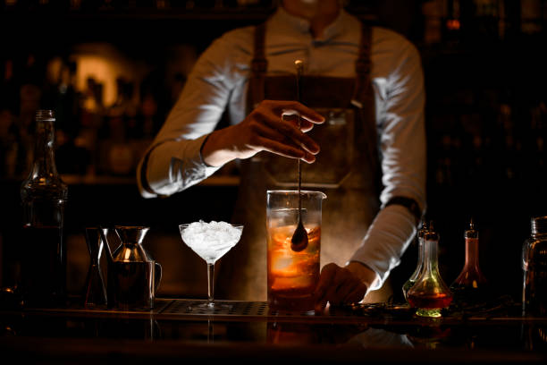 Bartender stirring alcohol cocktail with a spoon Male bartender in white shirt and leather apron stirring alcohol cocktail with a special bar spoon service occupation photos stock pictures, royalty-free photos & images