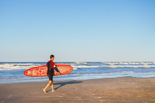 Rimini, Italy - 10 july, 2019: Surfer in diving suit with surfboard on beach in Rimini, Italy. Man after surfing in adriatic sea