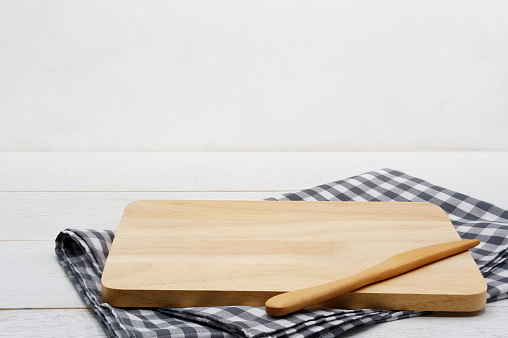 Empty rectangle wooden serving board with butter knife and grey gingham tablecloth on white wooden table.