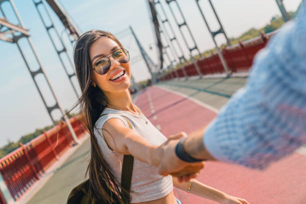 Follow me! appy young woman pulling guy's hand hand in hand walking on a bright sunny day on the bridge