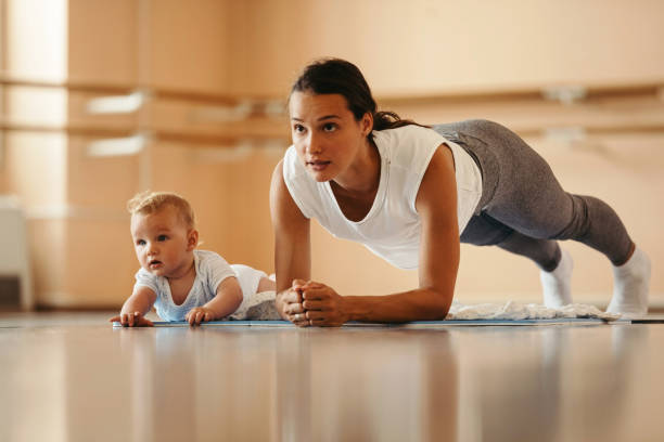 There is no excuse for her to get back in shape! Athletic mother exercising in plank position while being with her baby in a health club. Copy space. babyhood photos stock pictures, royalty-free photos & images