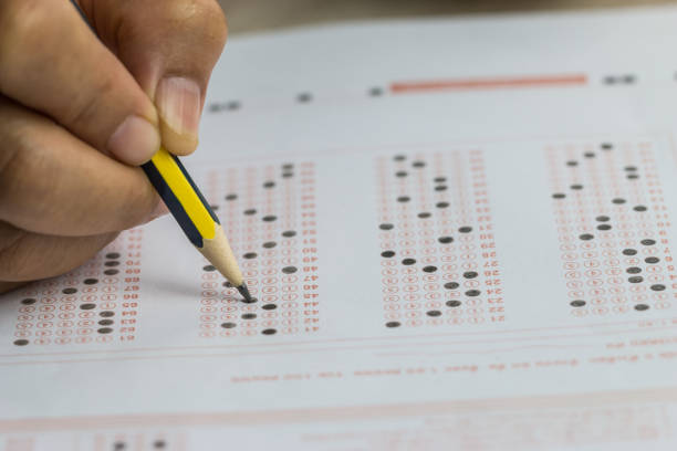 istock School or university students hands taking exams, writing examination room with holding pencil on optical form answers paper sheet on desk doing final test in classroom. Education assessment Concept 1164140473