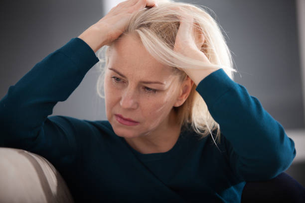 istock Sad depressed woman at home sitting on the couch, looking down and touching her forehead, loneliness and pain concept 1164141908