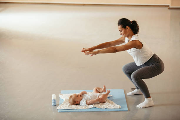 Athletic woman with baby doing squats on exercise class in health club. Young woman with baby practicing squats and getting in shape after the pregnancy. Copy space. baby squatting stock pictures, royalty-free photos & images