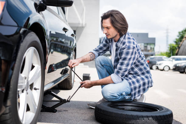 istock man in casual wear using jack tool and changing broken wheel on auto, car insurance concept 1164144079