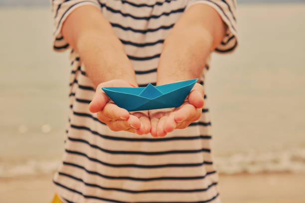istock Man holding paper boat on tropical beach. 1164147779
