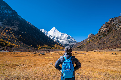 Woman standing with backpack on the Snow Mountain in daocheng yading,Sichuan,China.
