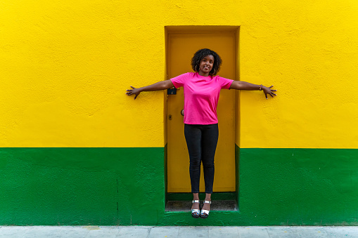 Beautiful young woman in pink t-shirt standing at a yellow and green doorway.