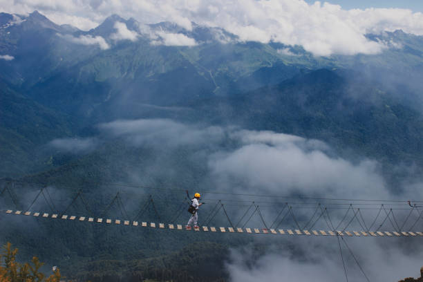 Extreme sports in the mountains people walk on the suspension bridge over the cliff in 2000 m. next to them, light clouds,which give the picture even more focusцель bridge crossing cloud built structure stock pictures, royalty-free photos & images