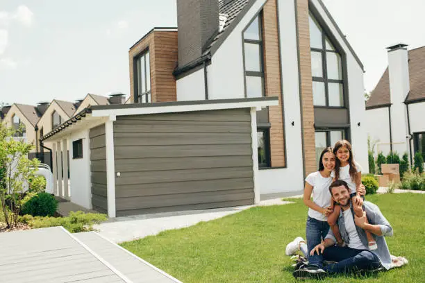 Photo of Family sitting on lawn in backyard, big modern house on background