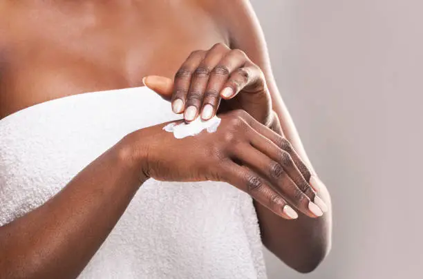 Photo of African girl applying body milk on her hand.