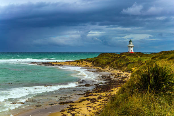 Early in the morning on a cloudy day at the Waipapa Point Lighthouse, a break in the cloud on the eastern horizon allows the warm glow of dawn to shine through, lighting up the lighthouse and some of the clouds.\nThe lighthouse is located in the Catlins area, on the south coast of New Zealand's South Island, east of Invercargill. It was built after the wreck of a passenger steamer cost 131 lives and was first lit on 1st January 1884. It was one of the last wooden lighthouses to be built in New Zealand and is a popular tourist destination for visitors to the area.