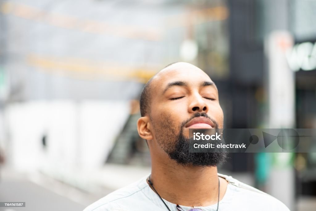 A moment of serenity A handsome man standing outside with his eyes closed, enjoying a moment of peace. Mindfulness Stock Photo