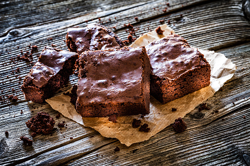 Homemade chocolate brownies shot on rustic wooden table. The brownies are on brown craft paper and brownie crumbles are scattered on the table. predominant color is brown. DSRL studio photo taken with Canon EOS 5D Mk II and Canon EF 100mm f/2.8L Macro IS USM.