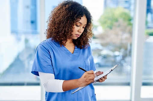 Shot of an attractive young female nurse writing notes on a clipboard at a hospital