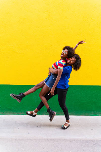 Playful sisters hugging by a yellow and green wall stock photo