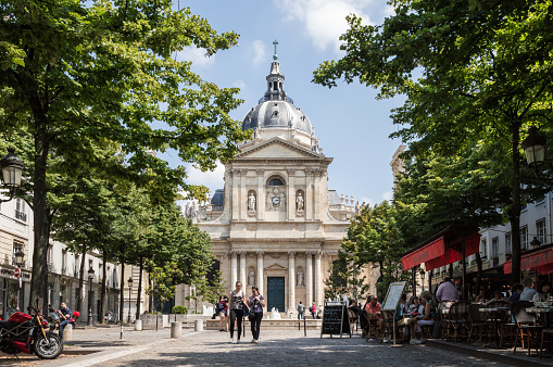 Paris - July 13th 2014: Horizontal view of the facade of the Sorbonne University surrounded with trees and restaurants.  Tourists walking nearby