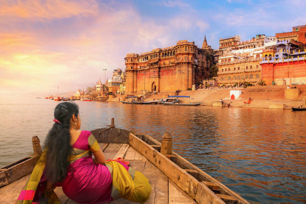 varanasi antike stadtarchitektur bei sonnenuntergang mit blick auf junge indische touristin genießen eine bootsfahrt auf dem fluss ganges - indian culture fotos stock-fotos und bilder