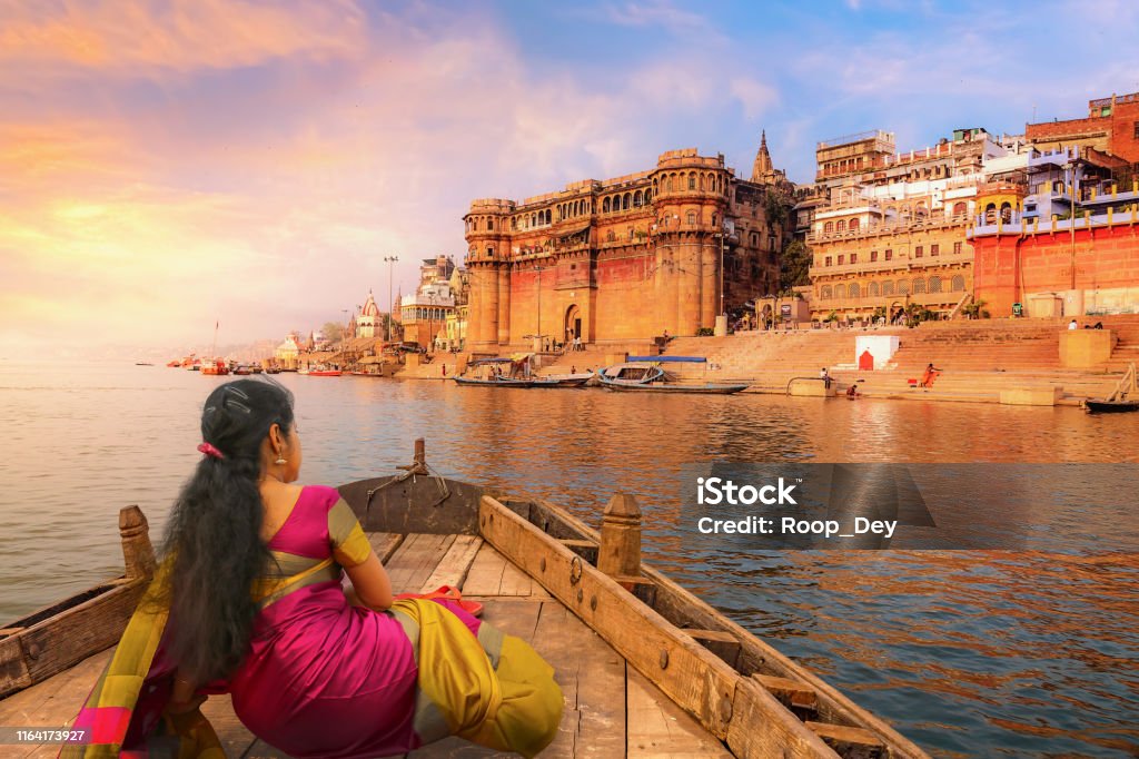 Varanasi ancient city architecture at sunset with view of young Indian female tourist enjoying a boat ride on river Ganges Varanasi ancient city architecture with Ganges river bank at sunset. Indian female tourist enjoy boat ride on the river Ganges and enjoy the view of historic Varanasi city architecture Varanasi Stock Photo
