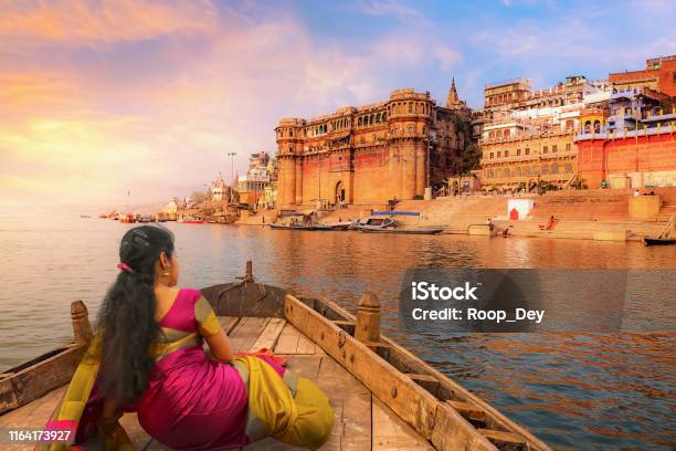 Varanasi Ancient City Architecture At Sunset With View Of Young Indian Female Tourist Enjoying A Boat Ride On River Ganges Stock Photo - Download Image Now