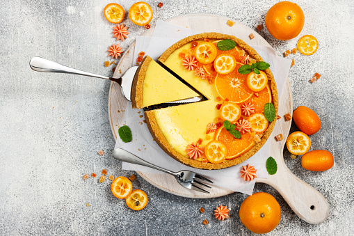 Cheesecake with slices of orange and kumquat on a gray stone background. Top view.