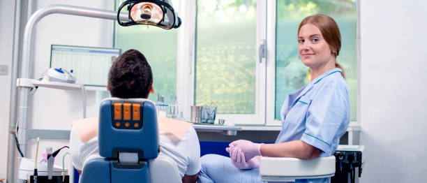 портрет улыбающегося дантиста и ее ассистента, стоящего рядом с пациентом в клинике. - dentist office audio стоковые фото и изображения
