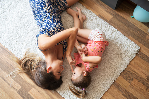 Mother and daughter lying on carpet and having fun at home.
